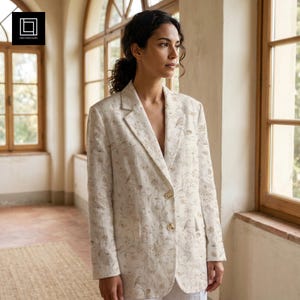 Op de afbeelding: Een beige blazer met een verfijnde, lichtbruine botanische print van ranken, bloemen en kleine vogels. Het kledingstuk heeft een reverskraag, lange mouwen, twee voorzakken en wordt aan de voorzijde gesloten met twee lichtgekleurde knopen.