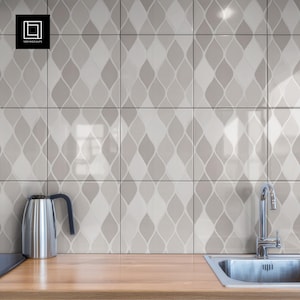May include: A kitchen scene featuring a stainless steel kettle and faucet. The backsplash is composed of square tiles with a repeating, light gray and white teardrop pattern. The countertop is made of light-colored wood.