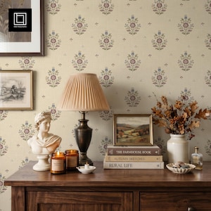 Pode incluir: Uma mesa consola de madeira exibe um candeeiro bege com abajur plissado, um busto branco, duas velas de vidro âmbar, uma pilha de três livros intitulados The Farmhouse Book, Autumn Sketches e Rural Life, e um vaso com folhagem seca.