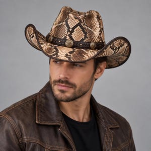 Puede incluir: Un sombrero de vaquero con un patrón de piel de serpiente en tonos marrón y bronceado, con una banda de cuero trenzado de color marrón oscuro. La banda está decorada con tachuelas metálicas circulares espaciadas con un diseño de estrella.
