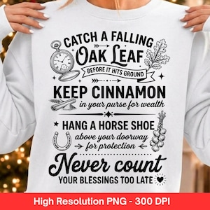 Peut inclure: Un sweat-shirt blanc avec du texte et des illustrations en noir. Le motif comprend une montre de poche, une feuille de chêne, un bâton de cannelle, un fer à cheval et une gousse d'ail, avec le texte Catch a falling oak leaf before it hits ground, Keep cinnamon in your purse for wealth, Hang a horse shoe above your doorway for protection, et Never count your blessings too late.