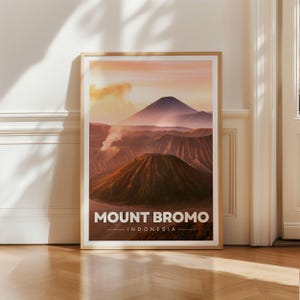 Peut inclure: Une affiche murale verticale encadrée représentant le paysage du mont Bromo en Indonésie. L'image montre un cratère volcanique aux pentes texturées sous un ciel aux tons doux et chauds. Le texte MOUNT BROMO INDONESIA est imprimé en blanc en bas.