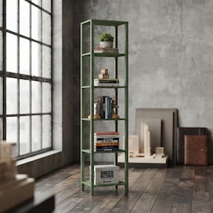 May include: A tall, narrow, sage green metal bookshelf with five open shelves. The shelves are filled with various items including a small potted plant, stacked books, decorative figurines, and a white storage box labeled with the text "TECH BOX".