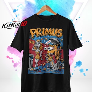 May include: A black t-shirt featuring a colourful graphic print with the text PRIMUS, O'MALLEY'S ALLEY, SAY BABY!, and June 26, 2018 Britt Pavilion Jacksonville, OR. The illustration depicts a cat-like character and a wild-eyed cat in a trash can.