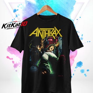 Puede incluir: Una camiseta negra de manga corta con un estampado gráfico del nombre de la banda Anthrax en letras amarillas sobre una ilustración de una persona en apuros. El diseño incluye tonos oscuros con acentos verdes y rojos en cuello redondo.