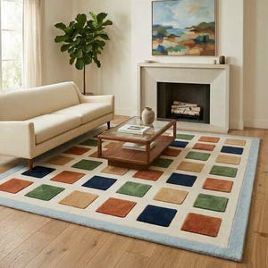 May include: A rectangular area rug featuring a cream-colored base with a grid of raised, square-shaped tufted patches in shades of navy blue, olive green, and terracotta orange, finished with a light blue border trim around the entire perimeter.