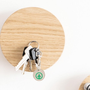 Op de afbeelding: Een ronde houten wandhaak met een sleutelbos eraan. De haak is gemaakt van lichtbruin hout en heeft een gladde, gepolijste afwerking.