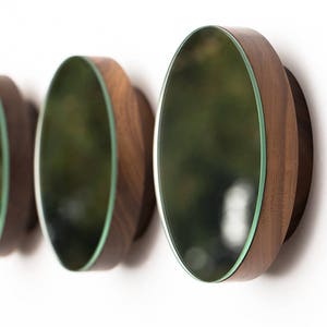 May include: Three round wooden wall mirrors with green glass inserts. The mirrors are arranged in a row, with the largest mirror on the right and the smallest mirror on the left.