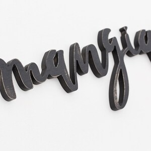 May include: Black wooden sign with the word "manja" written in cursive script.