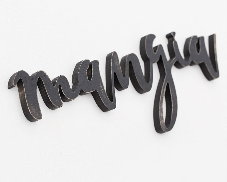 May include: Black wooden sign with the word "manja" written in cursive script.