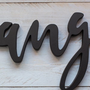 May include: Black wooden sign with the word "rang" written in a cursive font.