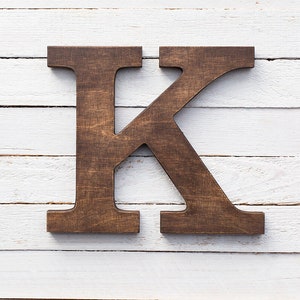May include: A dark brown wooden letter K on a white wood background.