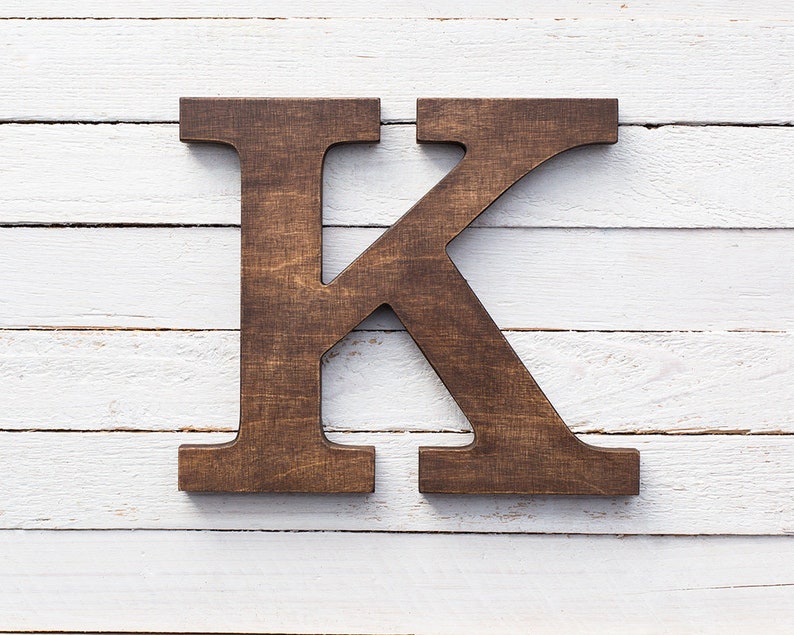 May include: A dark brown wooden letter K on a white wood background.