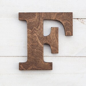 May include: A large, wooden letter F, painted in a dark brown color. The letter is made of solid wood and has a rustic, handcrafted look.