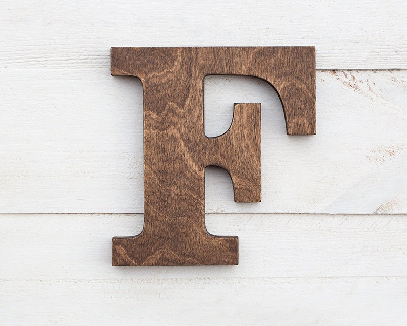 May include: A large, wooden letter F, painted in a dark brown color. The letter is made of solid wood and has a rustic, handcrafted look.