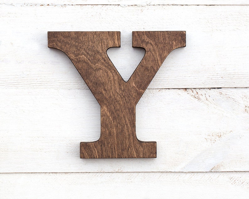 May include: A wooden letter Y, painted a dark brown color, is displayed against a white wood background.