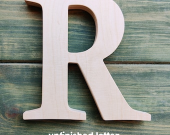 May include: Unfinished wooden letter R, in a light wood color, against a green wood background. The letter is standing upright and is ready to be painted or stained.
