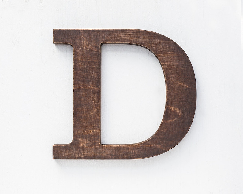 May include: A dark brown wooden letter D, standing upright on a white background.