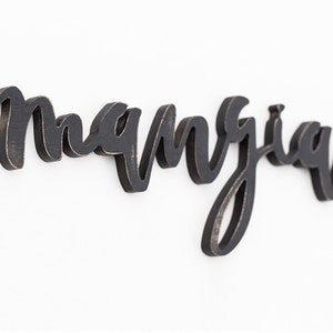 May include: Black wooden sign with the word "manjua" written in cursive script.