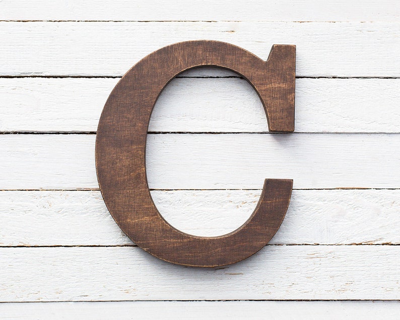 May include: A dark brown wooden letter C on a white wood background.