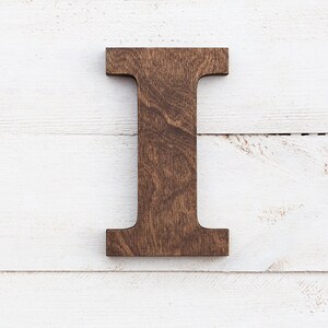 May include: A dark brown wooden letter I, standing upright against a white wood background.