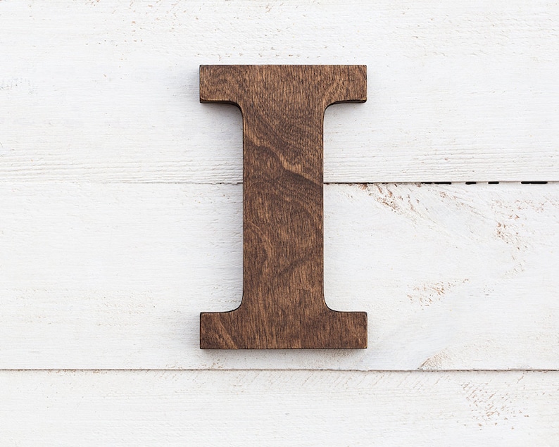 May include: A dark brown wooden letter I, standing upright against a white wood background.