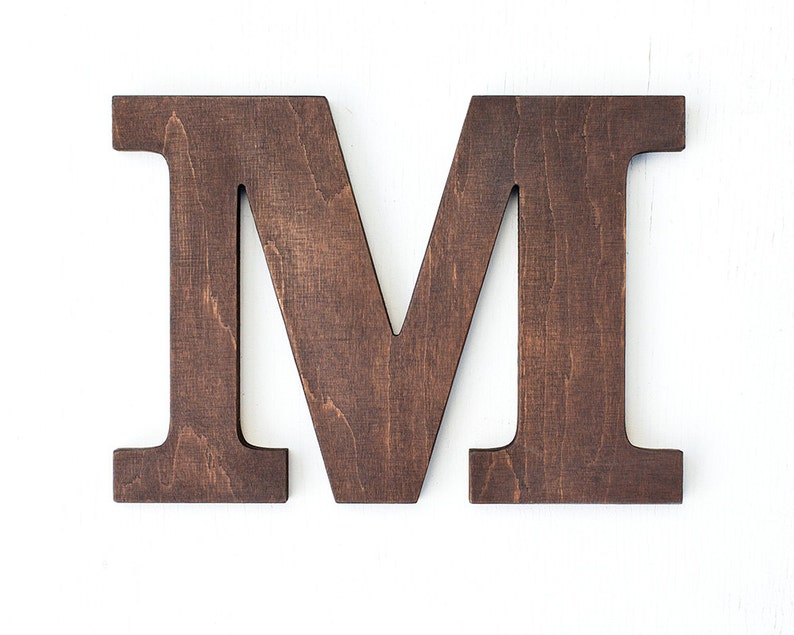 May include: A dark brown wooden letter M. The letter is made of wood and has a rustic finish.