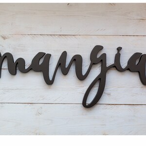 May include: Black wooden sign with the word "mangia" written in cursive script.