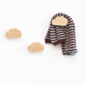 May include: Three wooden cloud-shaped hooks mounted on a white wall. A brown and gray striped scarf is hanging on one of the hooks.