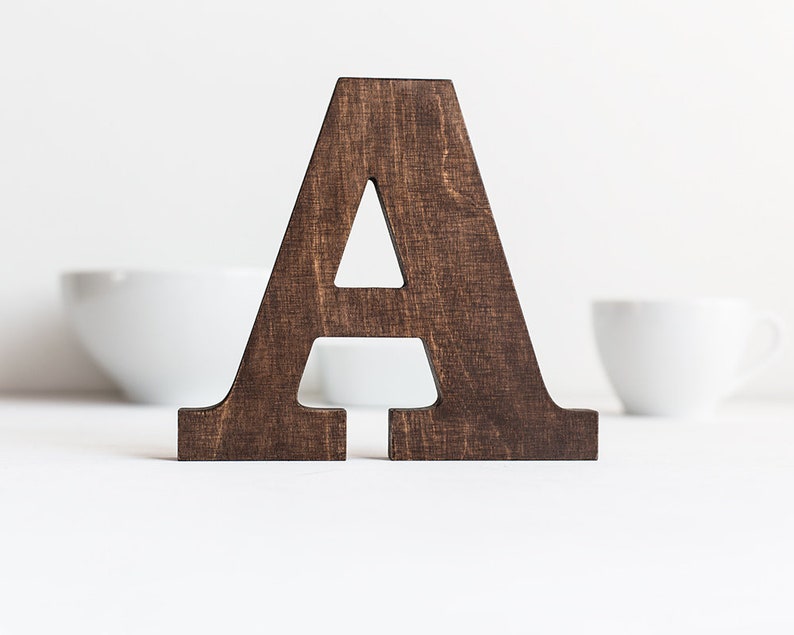 May include: A dark brown wooden letter A, standing on a white surface.