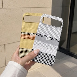 Könnte beinhalten: Zwei rechteckige Smartphone-Hüllen mit Karomuster und horizontalen Streifen. Eine Hülle ist gelb und orange, die andere weiß und grau. Beide Hüllen haben eine große horizontale Aussparung an der Oberseite und ein weißes G-Logo.