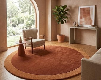 Puede incluir: Una alfombra circular grande que presenta un centro de color terracota intenso rodeado por un borde de color naranja quemado más claro. La alfombra está hecha de un material textil de color sólido con un pelo suave y uniforme.