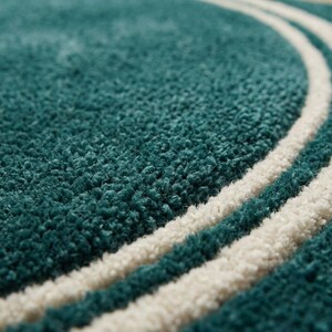 May include: A deep teal rug with a thick, high-pile texture featuring two parallel, curved white lines that sweep across the surface. The rug has a soft, tufted appearance with a consistent, dense weave throughout the entire visible area.