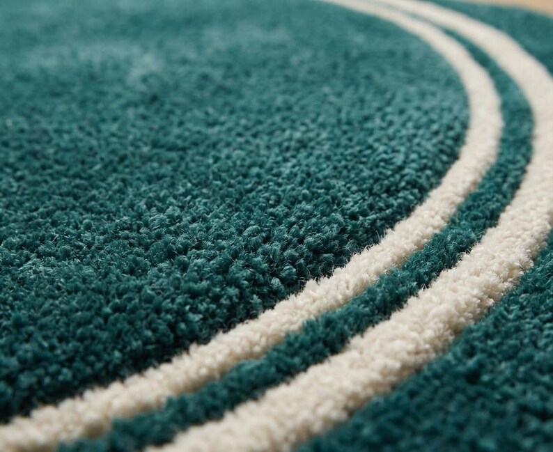 May include: A deep teal rug with a thick, high-pile texture featuring two parallel, curved white lines that sweep across the surface. The rug has a soft, tufted appearance with a consistent, dense weave throughout the entire visible area.