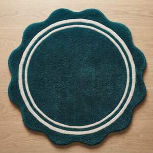 May include: A round, teal-colored rug with a scalloped edge and a double white circular border. The rug features a plush, textured surface and a consistent deep teal hue throughout the center, framed by two concentric white rings near the perimeter.