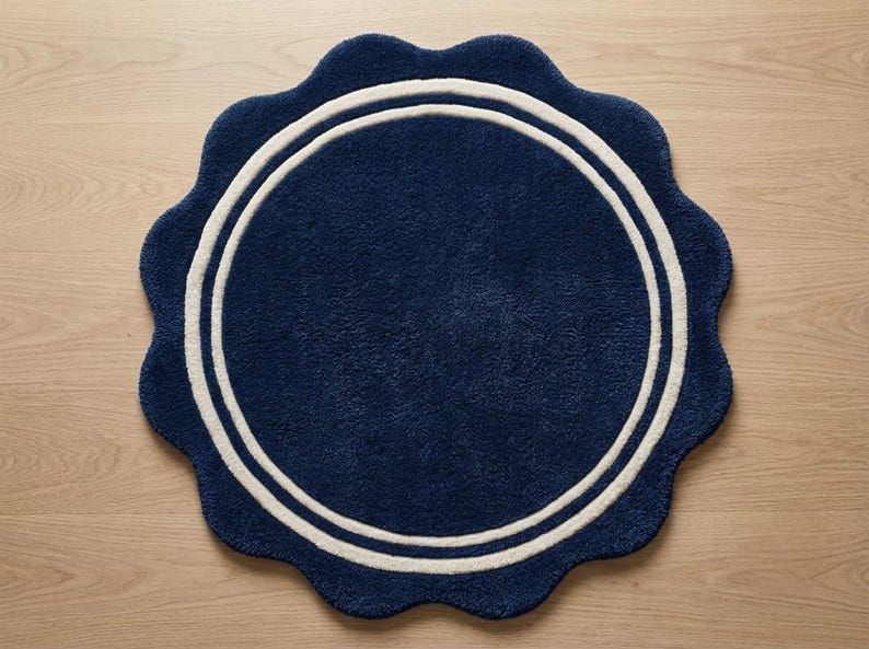 May include: A circular rug with a scalloped edge, featuring a deep navy blue color and two concentric white rings near the perimeter. The rug has a thick, tufted texture throughout its surface, creating a soft and plush appearance for floor decor.