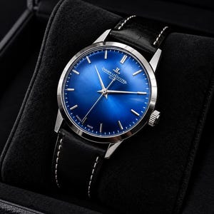 May include: A Jaeger-LeCoultre wristwatch with a vibrant blue sunray dial, silver-tone hour markers, and slender hands. The watch features a polished stainless steel case and a black leather strap with white stitching, presented in a box.