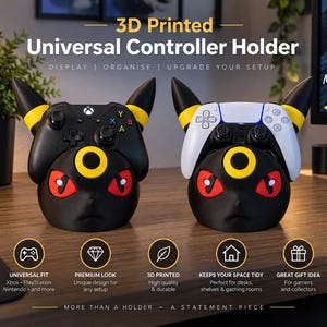 May include: Two 3D printed universal controller holders shaped like black creatures with yellow ear accents, red eyes, and yellow forehead rings. One holder supports a black Xbox controller, while the other holds a white PlayStation controller.
