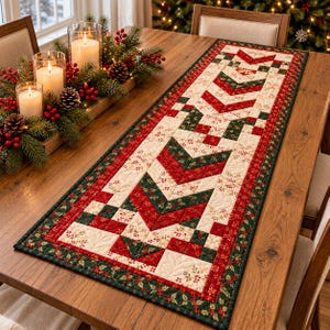 May include: A rectangular quilted table runner featuring a geometric chevron pattern in red, dark green, and cream. The fabric displays small holly leaf and berry prints, with intricate stitching details throughout the textile surface.
