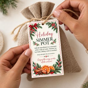 Peut inclure: Une étiquette rectangulaire blanche à bords festonnés rouges, ornée de branches de pin vertes, de baies rouges, de bâtons de cannelle et de tranches d'orange. Le texte indique : Holiday SIMMER POT, des instructions et Enjoy the cozy scents of the season!