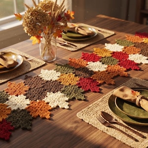 Pode incluir: Um caminho de mesa de crochê com um padrão repetitivo de folhas de bordo em tons de vermelho, laranja, amarelo, marrom, creme e verde-oliva. O caminho está disposto sobre uma mesa de madeira com pratos e um vaso de vidro com flores.