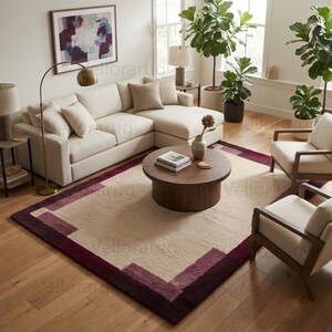 May include: A rectangular area rug featuring a large cream-colored center bordered by thick, geometric bands in shades of deep burgundy and muted plum. The rug has a textured, plush pile and is positioned on a light-toned wooden floor in a living room.