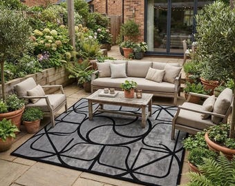 May include: An outdoor patio furniture set featuring a light gray sofa and two matching armchairs with beige cushions, arranged around a rectangular wooden coffee table on a large gray area rug with a bold black geometric pattern on stone tiles.