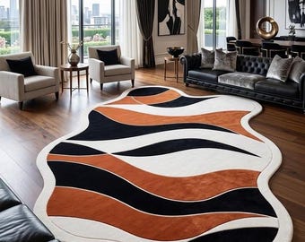 May include: An irregularly shaped area rug featuring a flowing, organic design with bold, wavy bands of burnt orange, deep black, and cream white. The rug has a thick, textured border in cream white that follows its unique, non-rectangular contour.