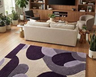 May include: A rectangular area rug featuring a high-pile texture with an abstract pattern of overlapping circular and curved shapes in shades of deep purple, light lavender, and cream, laid flat on a light-toned wooden floor.