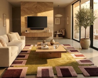 May include: A rectangular area rug featuring a central olive green field surrounded by a border of alternating light pink and deep burgundy geometric rectangular blocks, placed in a living room with a light-colored sofa and wooden coffee table.