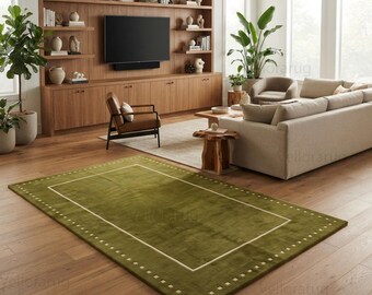 May include: A rectangular area rug in a deep olive green color featuring a thin white rectangular border accented with a repeating pattern of small white squares along the perimeter, placed on a light brown hardwood floor in a living room.