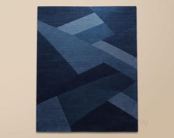 May include: A rectangular area rug featuring a geometric pattern of overlapping shapes in various shades of deep navy blue and lighter slate blue. The design consists of sharp, angular lines and solid color blocks. The text Vellorag is visible.