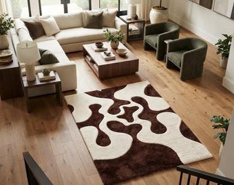 May include: A rectangular area rug featuring a high-pile texture with an abstract, organic pattern of interlocking dark brown and cream-colored shapes. The rug is positioned on a light-toned wooden floor in a living room setting.