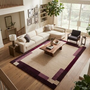 May include: A rectangular area rug featuring a large cream-colored center panel framed by a wide border in shades of deep burgundy and plum. The rug has a textured pile and is positioned on a light-toned wooden floor in a living room setting.